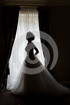 Beautiful delicate bride happy woman with a crown on her head by the window with a large wedding bouquet in a luxurious white