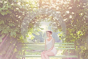 Beautiful delicate elegant woman bride in white dress with hair and tiara on his head sitting in a lush garden on a bench under