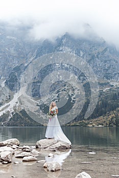 Beautiful delicate girl in the air blue bride wedding dress with luxurious curls in the mountains near the lake with a wedding bou