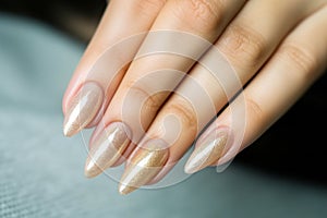 Beautiful delicate manicure. Long almond shaped nails. Close-up of a hand of a woman with a gentle golden sparkling gel varnish