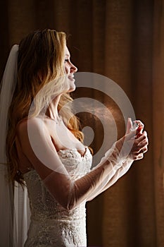 a beautiful, delicate and sexy blonde bride in a veil uses perfume