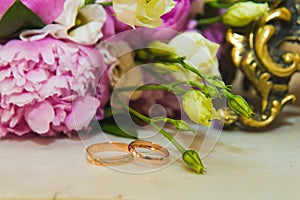 Beautiful delicate wedding bouquet of pink peonies and wedding rings of the bride and groom