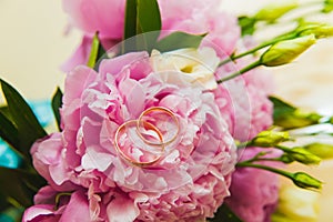 Beautiful delicate wedding bouquet of pink peonies and wedding rings of the bride and groom