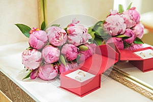 Beautiful delicate wedding bouquet of pink peonies and wedding rings of the bride and groom in a red box