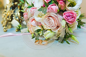 Beautiful delicate wedding bouquet of white and pink roses and wedding rings of the bride and groom.