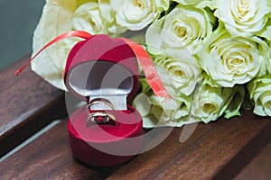 Beautiful delicate wedding bouquet of white roses and wedding rings of the bride and groom in a red box