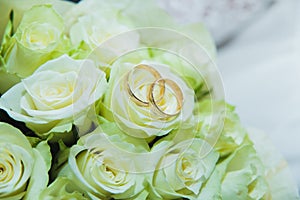 Beautiful delicate wedding bouquet of white roses and wedding rings of the bride and groom