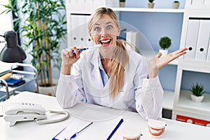 Beautiful dentist woman explaining how to brush teeth with toothbrush celebrating achievement with happy smile and winner