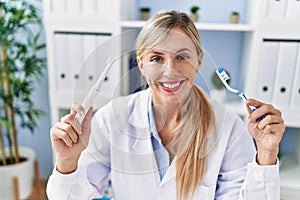 Beautiful dentist woman holding ordinary toothbrush and electric toothbrush smiling with a happy and cool smile on face