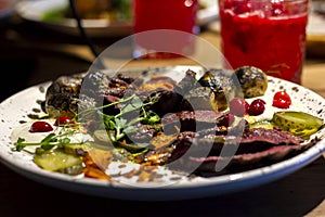 A beautiful dish with fried meat steak cut into slices and decorated with cranberries, cucumbers, herbs