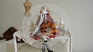 A beautiful doll sits on a shelf with a maple branch.