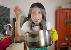 Beautiful domestic chef at work - lifestyle portrait of young pretty and happy Asian Chinese woman in apron holding cooking pot