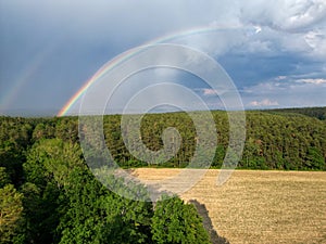 Beautiful double rainbow arching over field and forest with dark clouds and rain in the background