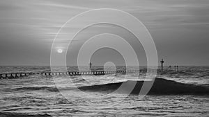 Beautiful dramatic black and white stormy landscape image of waves crashing onto beach at sunrise