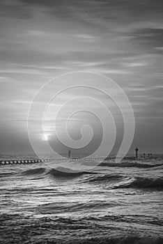 Beautiful dramatic black and white stormy landscape image of waves crashing onto beach at sunrise