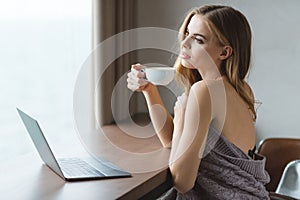 Beautiful dreaming young woman with laptop drinking coffe