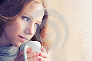 Beautiful dreamy girl with a cup of hot coffee at the window