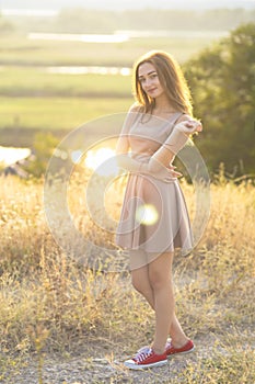 beautiful girl walking in a field in a dress at sunset, a young woman enjoying summer nature