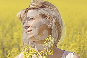 Beautiful dreamy woman in a rapeseed field with a bouquet dreams and enjoys nature.