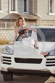 Beautiful driver girl model sitting on white bonnet of luxu photo