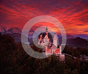 Beautiful early morning view of the Neuschwanstein fairy tale castle, bloody dark sky with autumn colours in the trees during