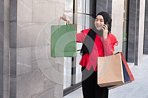 Beautiful East Asian Islamic women wearing hijab. Smile and feeling happy and holding many shopping bags walking in urban city