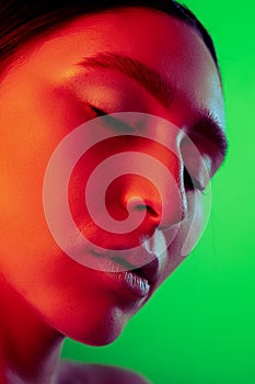 Beautiful east woman close up portrait isolated on green background in red neon light