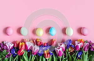 Beautiful Easter border with spring flowers and eggs on a pink background. Easter floral background. Copy space, top view, flat