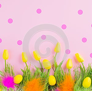 Beautiful Easter bright vivid spring blooming tulip flowers, colorful eggs, fresh grass and colourful feathers over pink polka dot