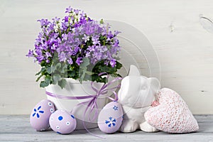 Beautiful Easter card with easter eggs, a pot of flowers and ceramic rabbit on a white wooden background