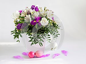 A beautiful Easter composition with a bouquet of flowers, pink painted chicken eggs and feathers on a white background