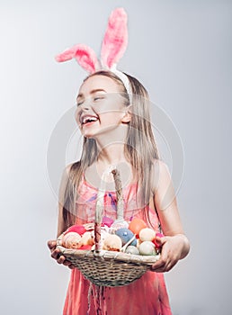 Beautiful Easter smiling little girl wearing bunny rabbit ears, child holding a basket full of colorful painted Easter eggs