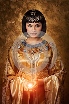 Beautiful Egyptian woman like Cleopatra with magic ball on golden background