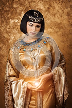 Beautiful Egyptian woman like Cleopatra with magic ball on golden background