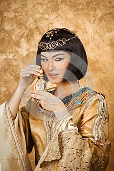 Beautiful Egyptian woman like Cleopatra with perfume bottle on golden background