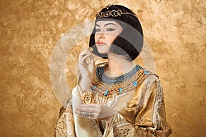 Beautiful Egyptian woman like Cleopatra with perfume bottle on golden background