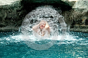 Beautiful elder mature adult sexy redhead woman under the splashing water in the Spa Wellness pool enjoys the falling water