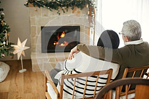 Beautiful elderly couple hugging and enjoying cozy fireplace in stylish christmas decorated living room. Cozy winter. Happy senior