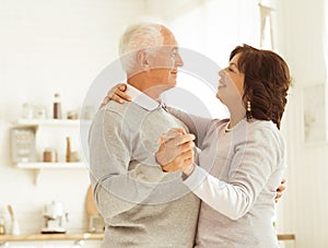 A beautiful elderly married couple is dancing in the room. Pensioners are happy together.