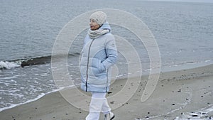 A beautiful elderly woman enjoys a frosty day while walking along the beach