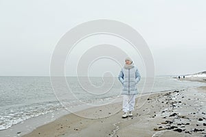 A beautiful elderly woman enjoys a frosty day while walking along the beach