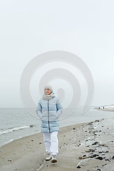 A beautiful elderly woman enjoys a frosty day while walking along the beach