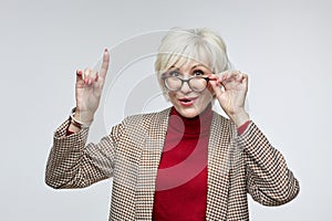 beautiful elderly woman with glasses shows her index finger up. advertising concept of a business woman leader