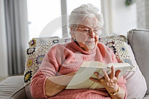 Beautiful elderly woman reading book at home, having relaxing moment, hygge for senior. Grandmother with reading glasses