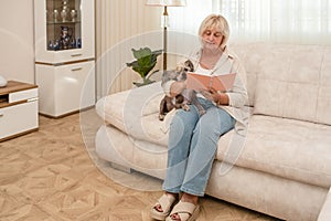 Beautiful elderly woman sitting on the couch in living room and writing in planner.