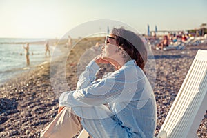 Beautiful elderly woman sitting in a deckchair on the beach and