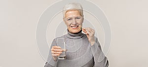 Beautiful elderly woman taking vitamin supplements over light studio background