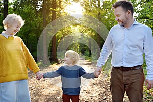 Beautiful eldery woman and her adult son, and her little grandson walking together in sunny summer park