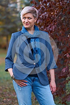 Beautiful elegant blond woman posing in autumn city park, dressed in blue jeans and jacket