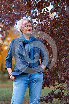 Beautiful elegant blond woman posing in autumn city park, dressed in blue jeans and jacket